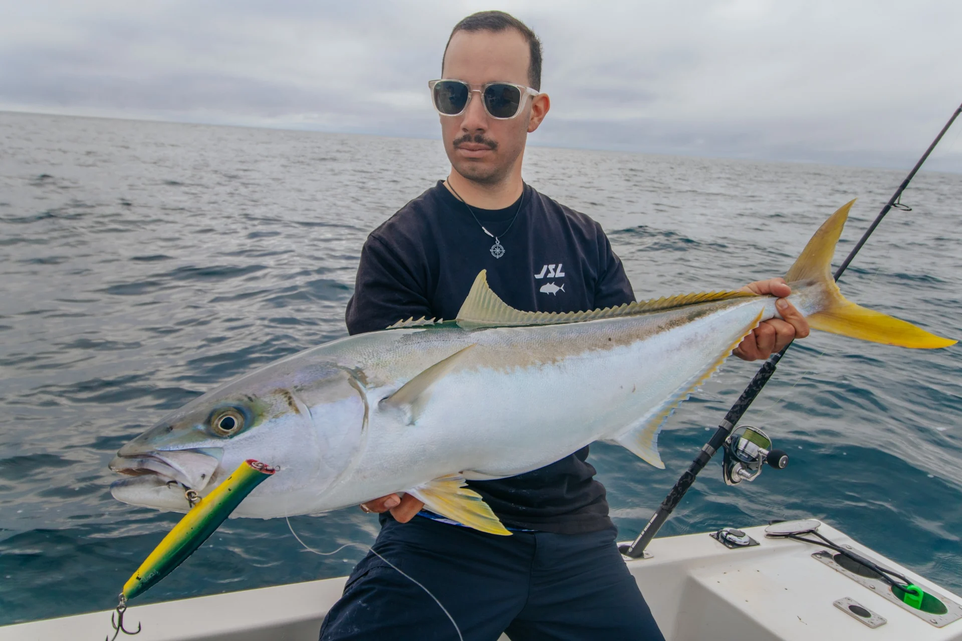 Angler holding a yellowtail kingfish with a green-and-yellow lure at its mouth.